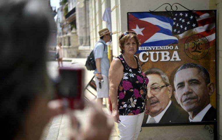 ulher cubana posa em frente a cartaz que destaca encontro entre Raúl Castro e Barack Obama. As coisas estão mudando.