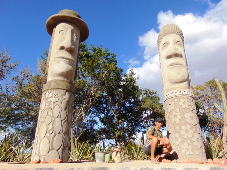 Agachado, o artista plástico, Severino Iabá. Em destaque os dois primeiros totens da sua obra, que simbolizam seus pais, Josefa Minervina e Jose Severino da Silva, ambos hoje com 79 anos | Foto: Surubim News 