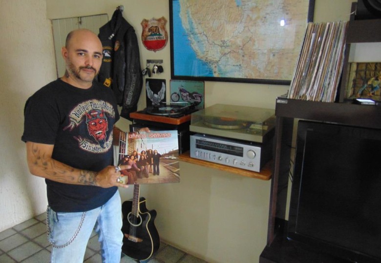 Rodrigo em casa, ao lado da sua vitrola, portando um vinil da banda americana Lynyrd Skynyrd, que fez muito sucesso nos anos 70. | Foto: Surubim News